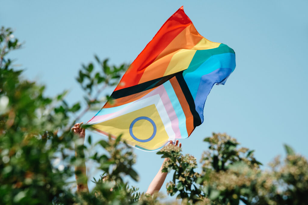 closeup of a person showing an intersex-inclusive progress pride flag peeping out from a bush. lgbtq+ youth and mental health